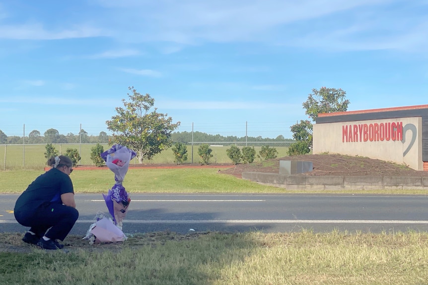 A woman in a nurses uniform places flowers by a roadside tribute.