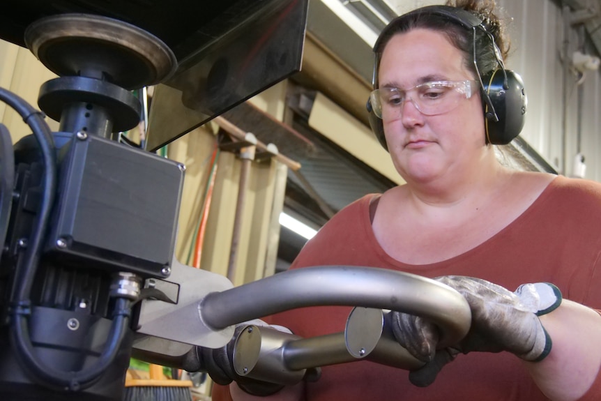 A woman wearing safety glasses and ear muffs operating a workshop machine.