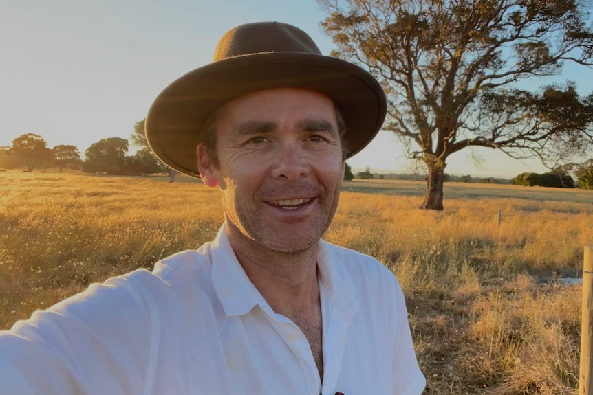 A happy man in a hat stands in a field.