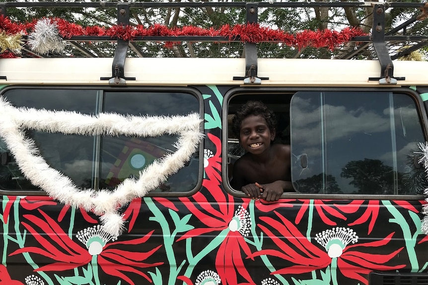 A child smiles out the window of the car in Maningrida