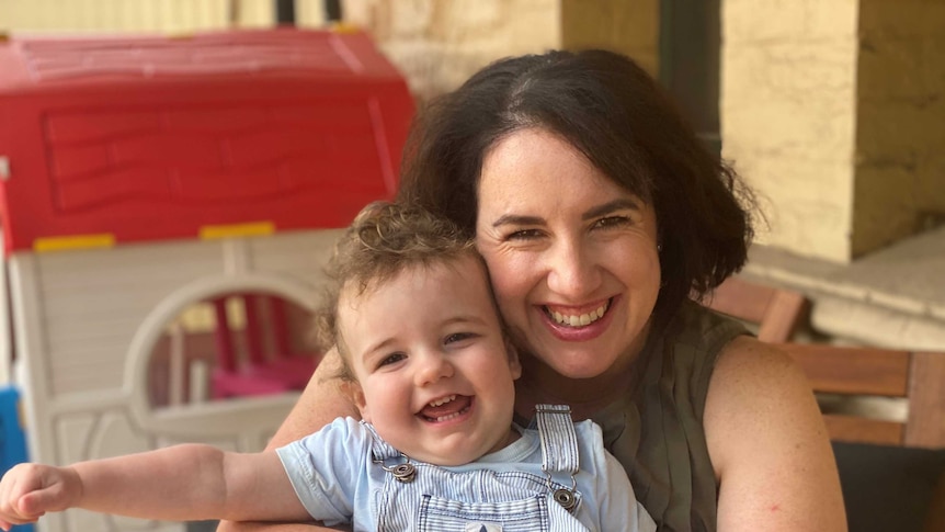 A toddler sits on his mother's lap being hugged tightly. Both are smiling.