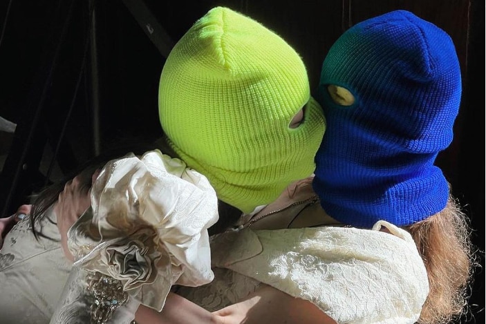 Two women in brightly coloured ski masks kiss