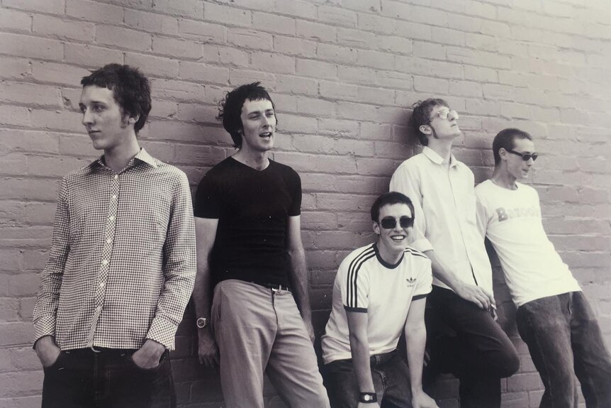 A black and white photo of five-piece The Panics standing in front of a brick wall