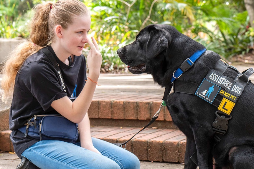 A teenage girl locks eyes with a black labrador dog.