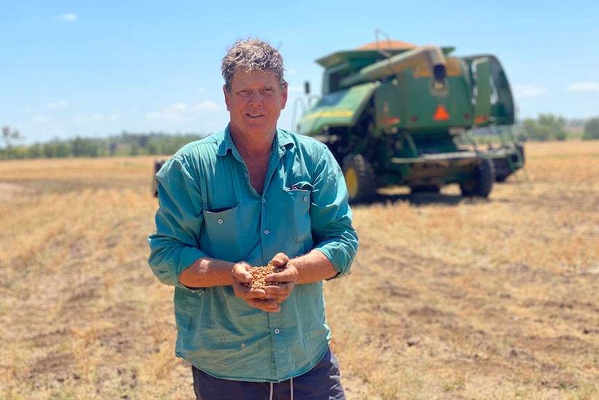 Neal Johansen standing in a long sleeved blue shirt holding chickpea, machinery behind.