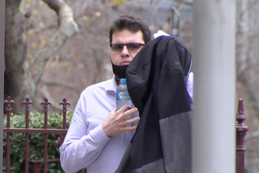 Mitchell Landry holds a coat up to obscure his face as he walks, dressed in a purple business shirt, along a CBD footpath.