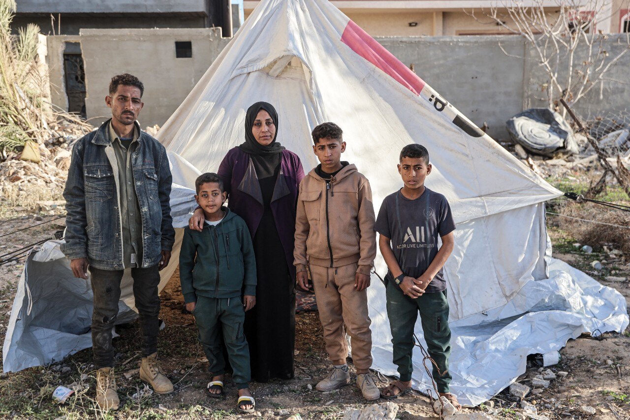 Two adults and three children standing near a tent, looking at the camera, with serious expressions on their faces.