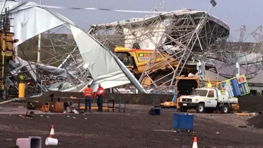 A very large shed is reduced to rubble, with a big mine dumper truck under the debris