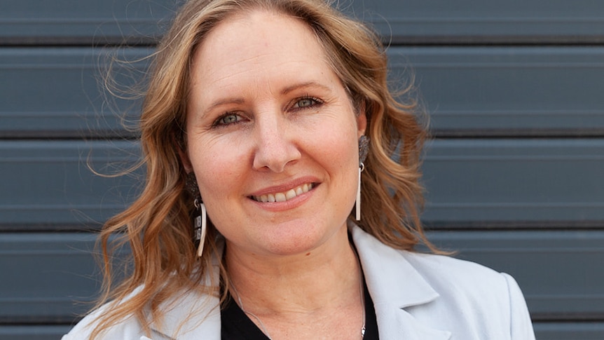 Woman wearing pale suit and dark shirt looks at camera