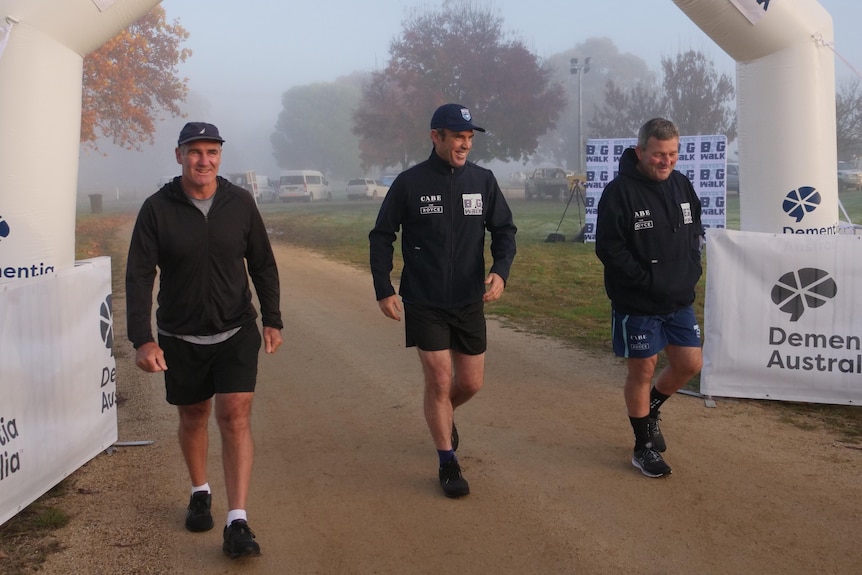 Three men standing on a dirt track. 