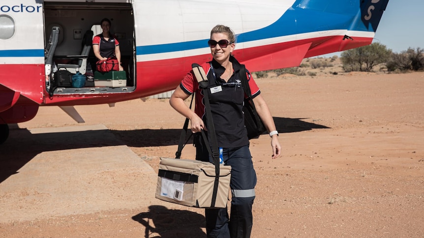 A woman walks off a plane with a wheelie case