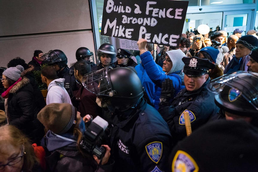 Protesters are surrounded by police officers and travellers at JFK.