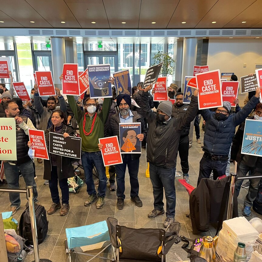 A crowd of people holding placards displaying slogans including 'end caste discrimination' and 'justice'.