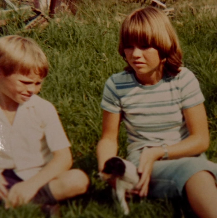 Foto antiga de duas crianças sentadas na grama e segurando um cachorrinho.