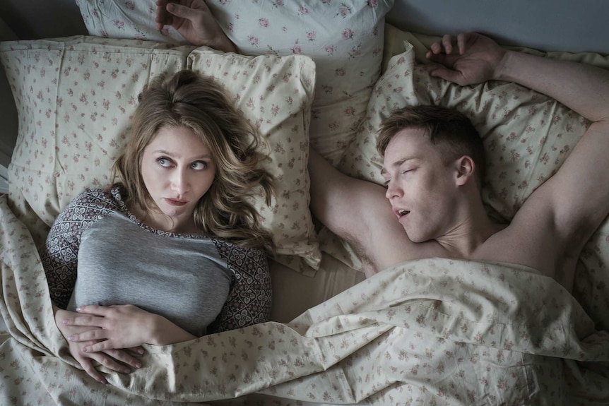 An awake woman and sleeping man lying in bed