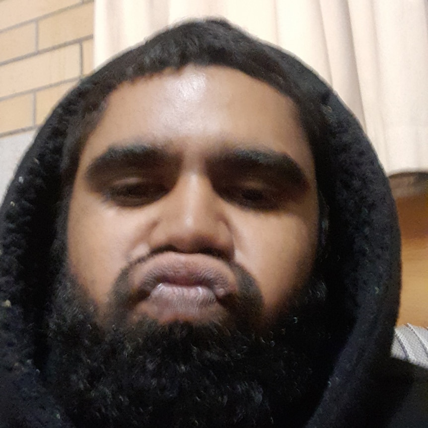 A man with black hair and a beard with a hoodie over his head making a face