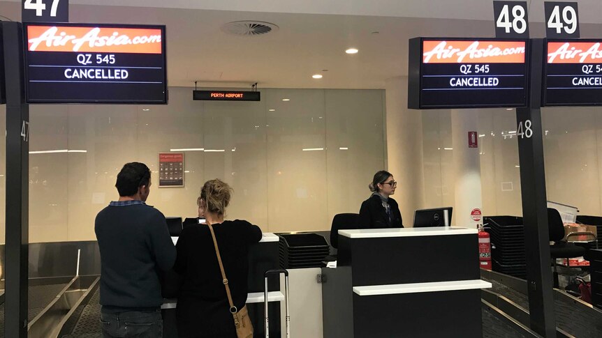 Two people in front of a check-in counter at Perth airport showing Air Asia flight cancelled.