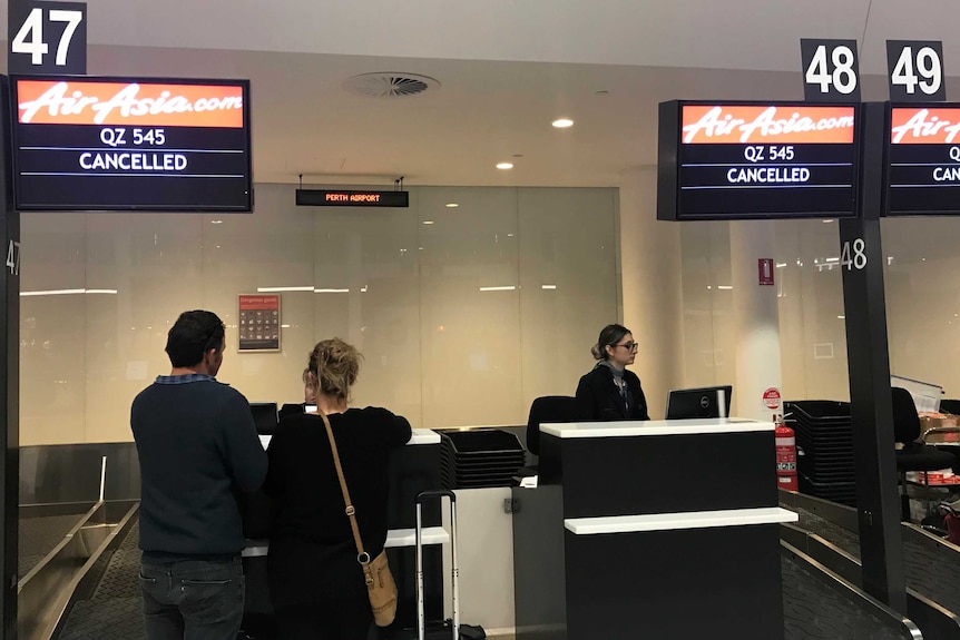 Two people in front of a check-in counter at Perth airport showing Air Asia flight cancelled.