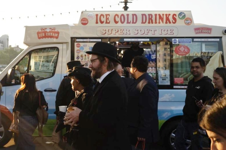 crowds walk in front of an ice cream van