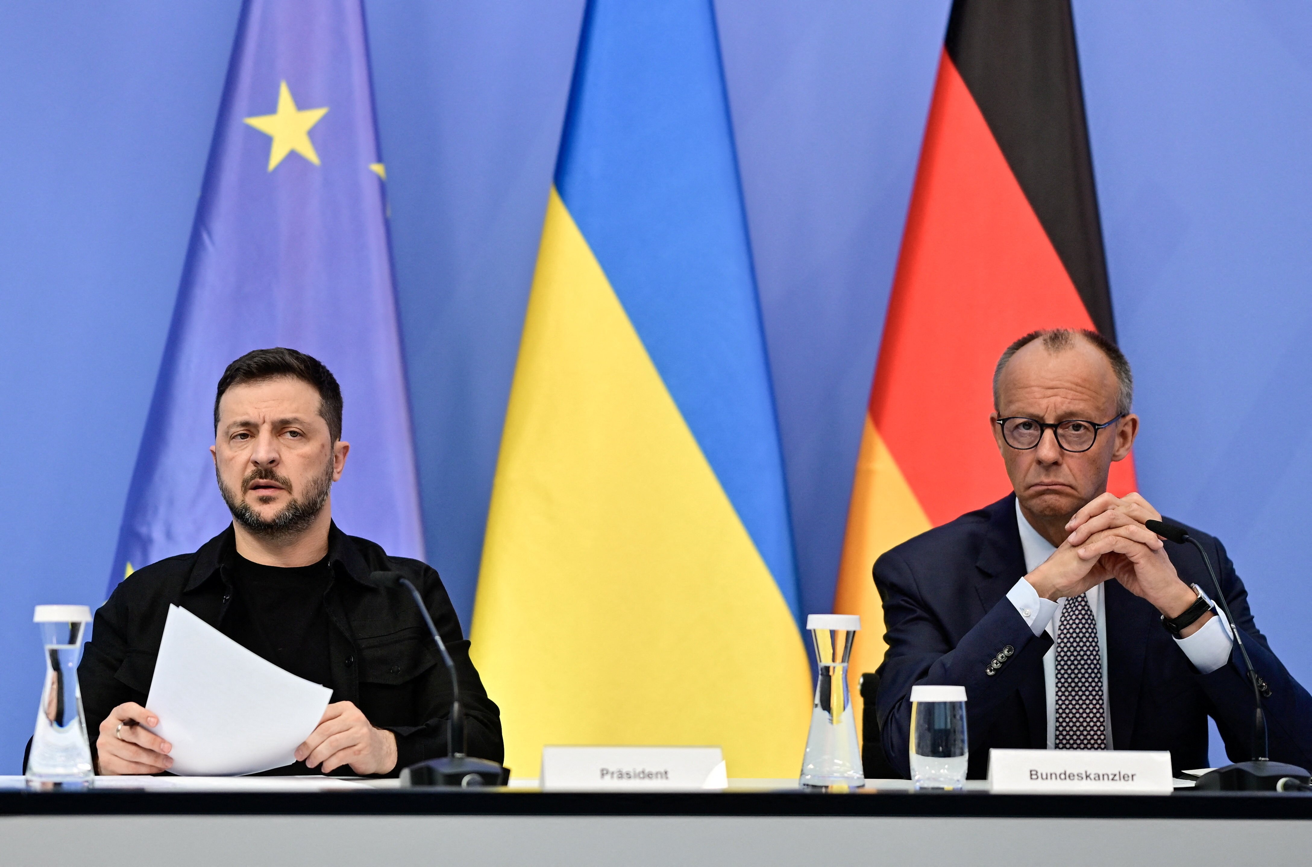 Two man sit at a desk with a Ukraine, EU and German flag behind them 