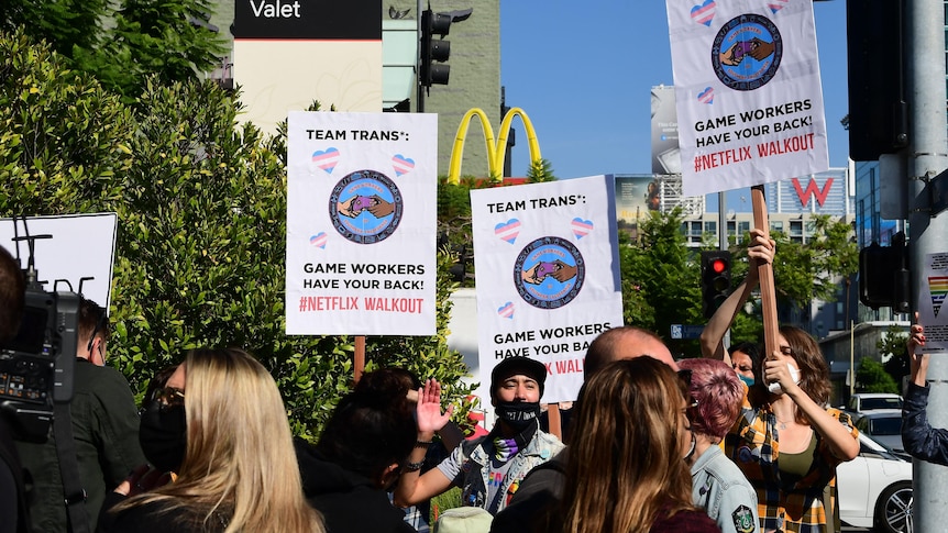 protesters hold up 'team trans' signs outdoors