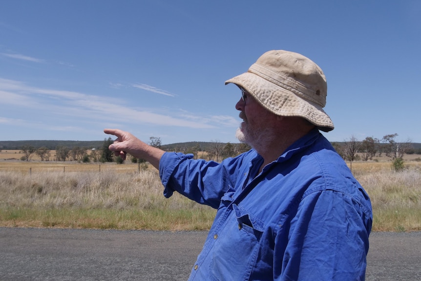 A man wearing a hat points to a paddock from the road side.