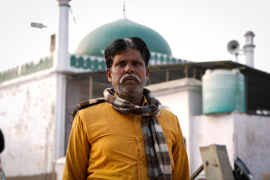 A man wearing yellow shirt and a scarf stands outside a mosque