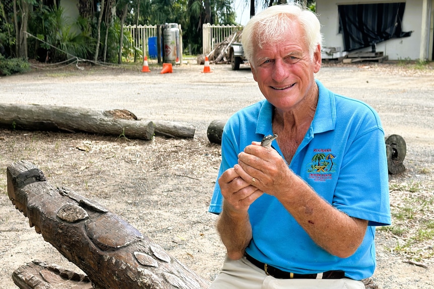 A man wearing a blue shirt holding a baby crocodile.