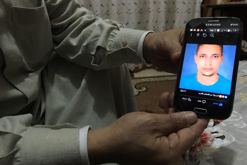 A man holds up a phone with a photo of his son
