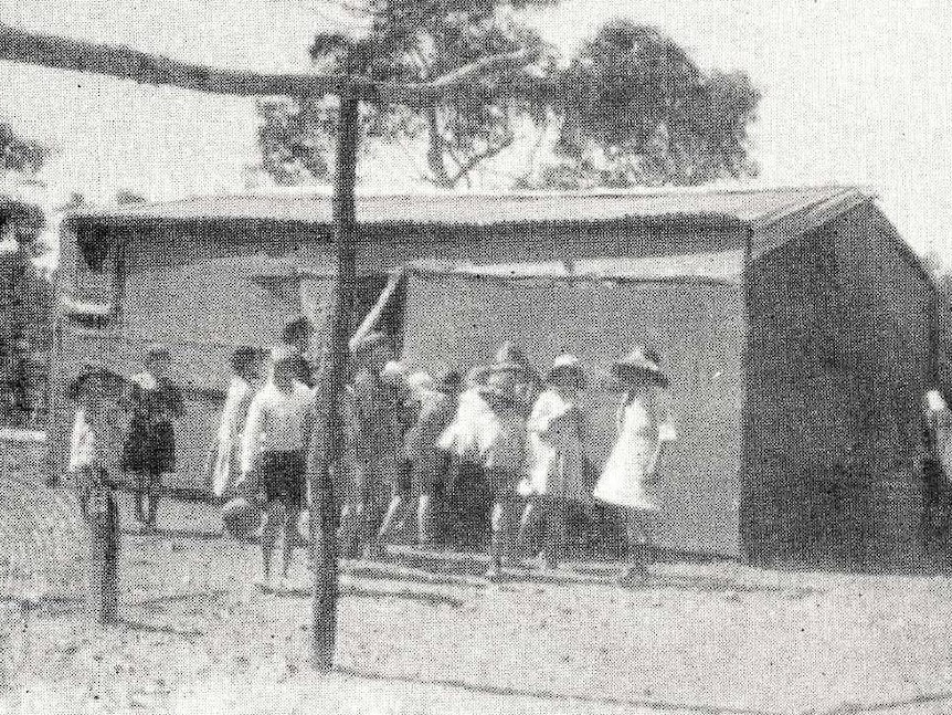 Black and white image of old shed with people standing in front of it