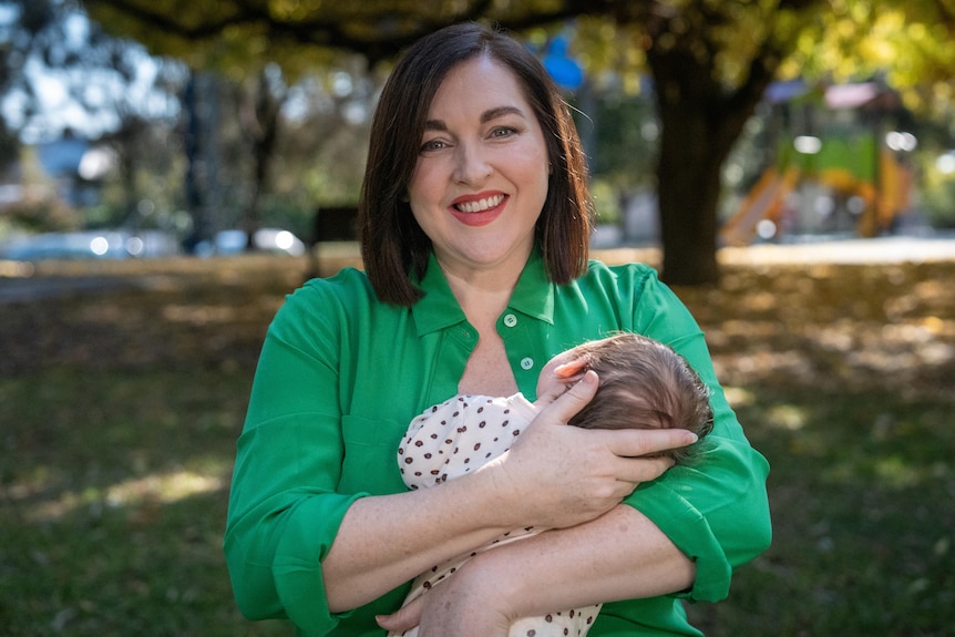 MP Jayne Stinson smiles as she holds a young baby with brown hair who is snuggled in to her chest