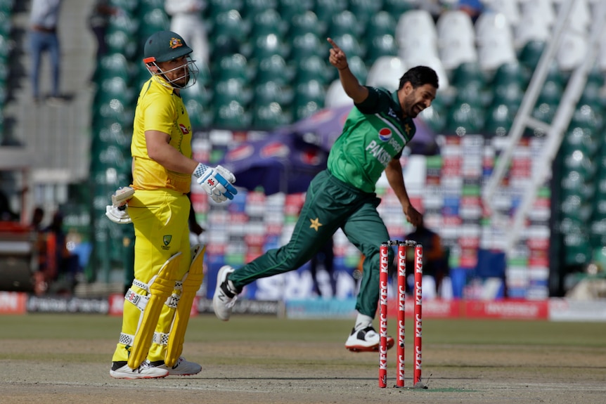 An Australian ODI cricketer looks dejected after being given out as a bowler runs away with arms out in celebration.