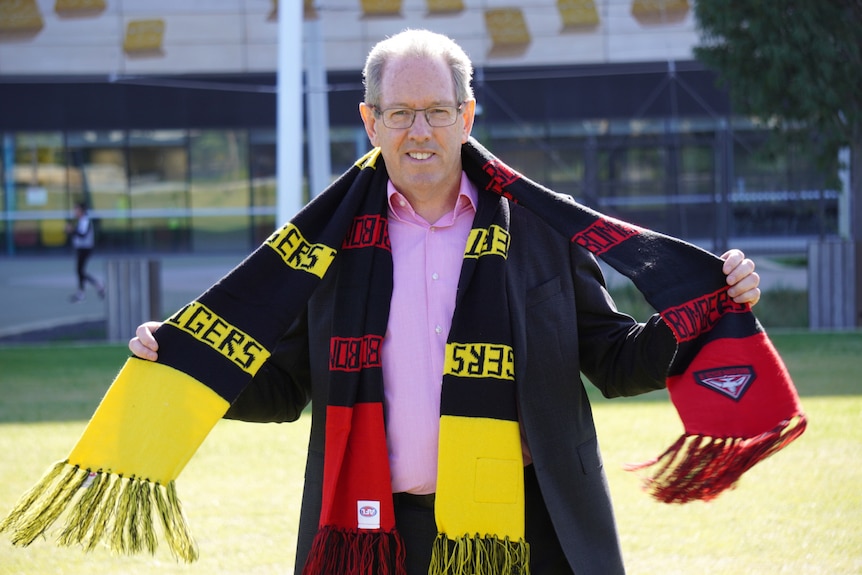 A man wearing two football scarves smiles at the camera.