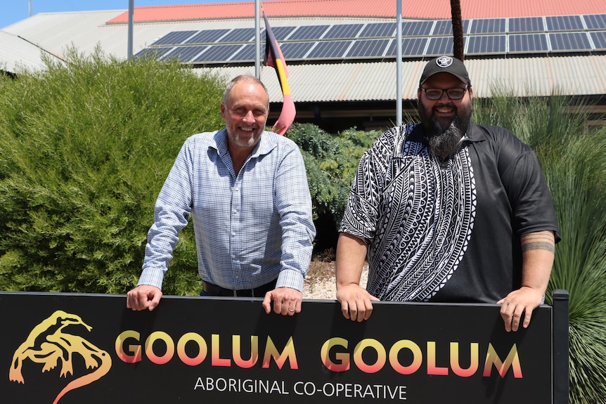Two people leaning on a sign bearing the words 'Goolum Goolum' and facing the camera.
