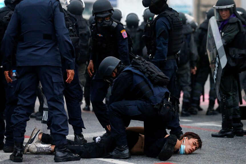 A police officer pins a protester to the ground during rallies against the government in Bangkok