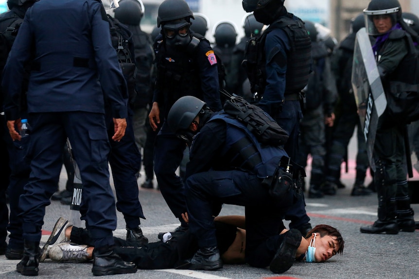 A police officer pins a protester to the ground during rallies against the government in Bangkok