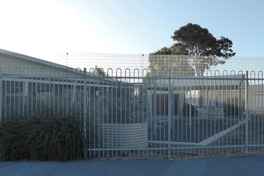 Fenced area at back of building, trees and bushes on left and in background
