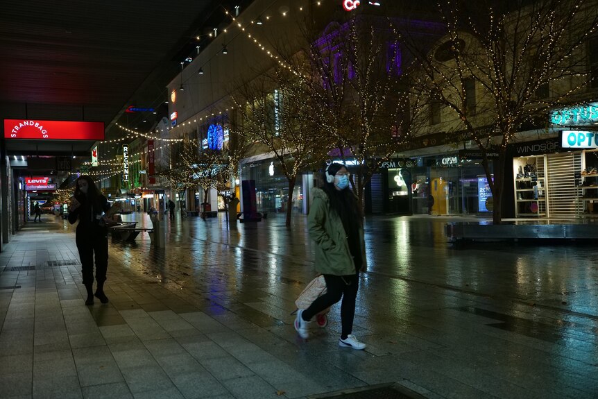 People wearing masks during an empty pedestrian mall at night