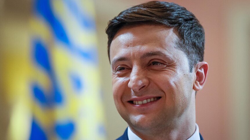 Volodymir Zelenskiy, dressed in a suit, smiles to the left of frame