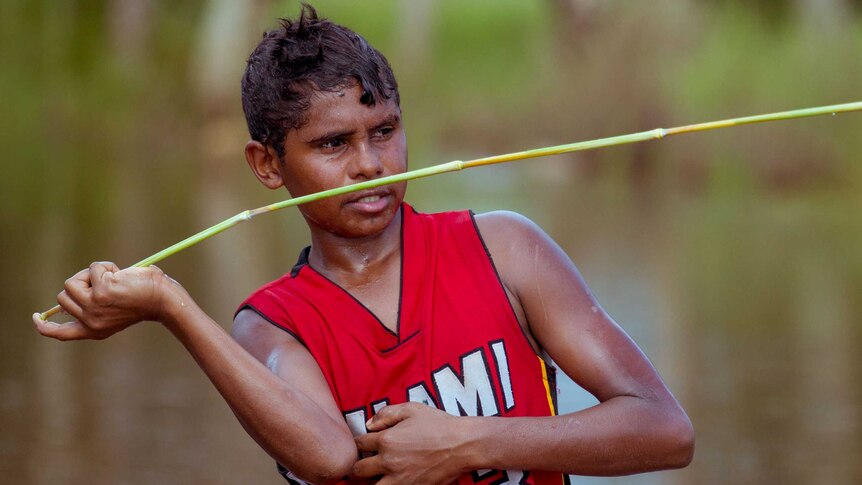 Junior Dirdi holds vegetation, shaped like a spear