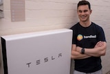 man in shirt standing next to white electricity box that reads Tesla
