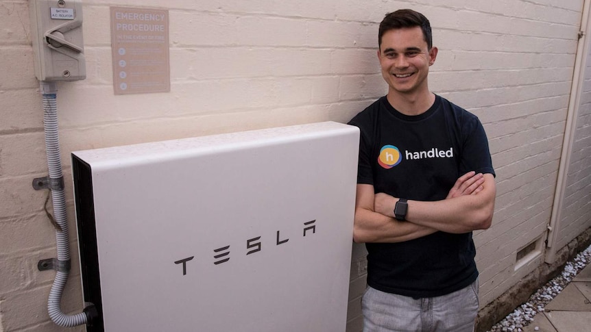 man in shirt standing next to white electricity box that reads Tesla