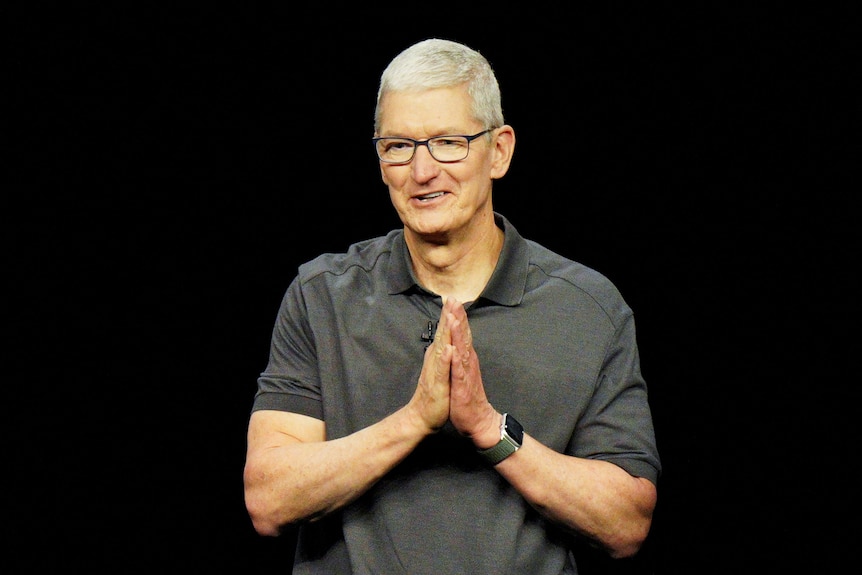 A white man with glasses, short hair and a polo shirt smiles with his hands together in front of his chest.