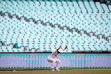 A cricketer stretches in front of empty seats at the SCG