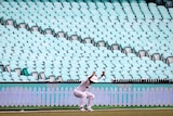 A cricketer stretches in front of empty seats at the SCG