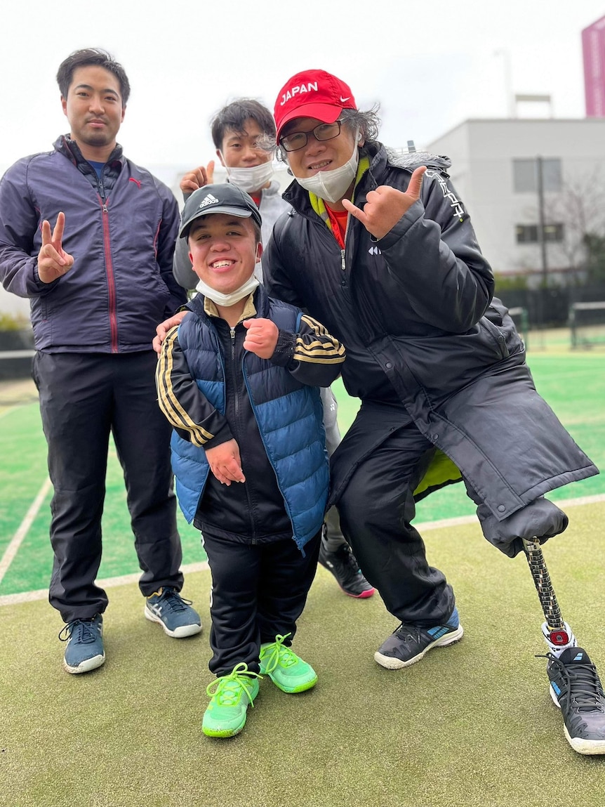 A young man with dwarfism, standing with three Japanese men, one who has a prosthetic leg
