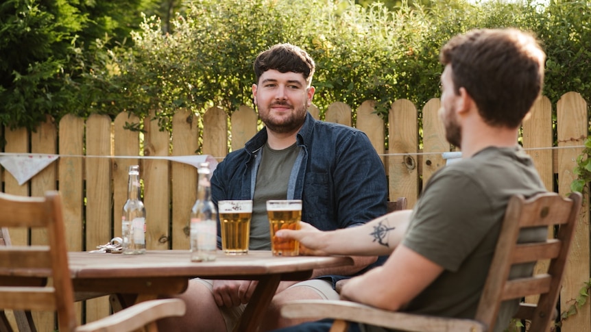 Two young men sitting at a table outside drinking beer.