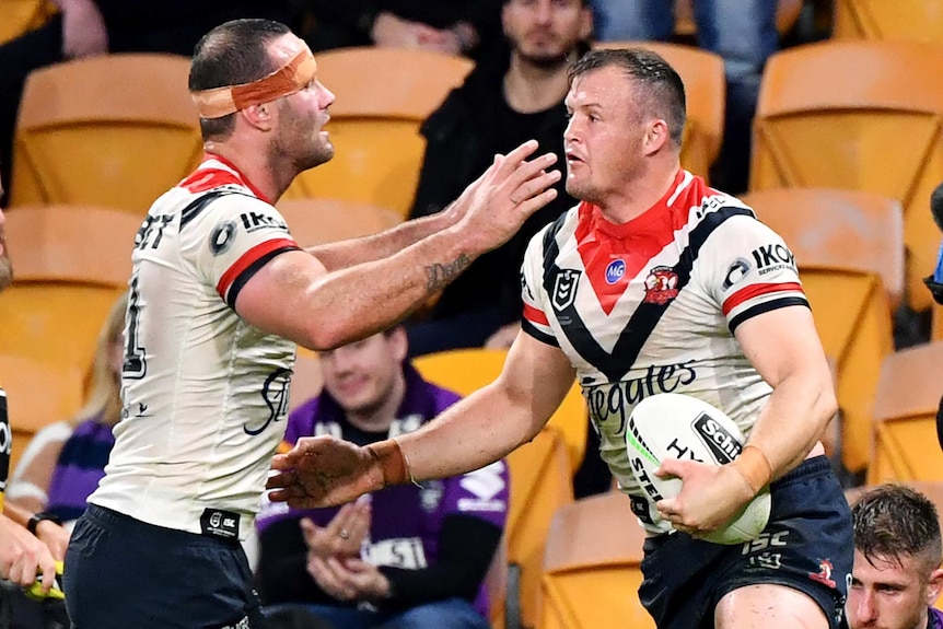 A Sydney Roosters NRL player is congratulated by a teammate as he holds the ball after scoring a try against Melbourne.