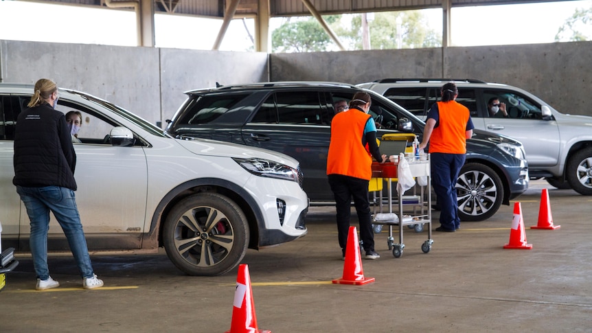 Three cars lining up in a pavilion with healthworkers tending to them