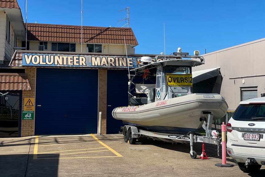 A boat on a trailer parked outside a shed with a sign 'volunteer marine' 